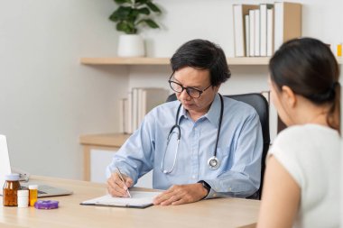 Bir doktor, modern bir muayenehanede hastaya danışmanlık yaparken sağlık ve sağlığa odaklanarak notlar yazar..