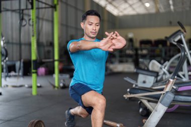 Kendini spora adamış bir adam, yoğun bir idmana hazırlanmak ve kuvvet eğitimini vurgulayarak bir spor salonunda hamleler yapar..