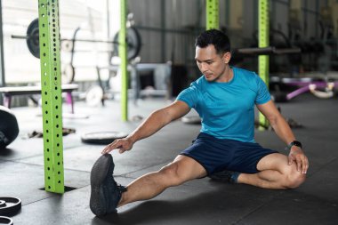 Kendini spora adamış bir fitness meraklısı spor salonunda otururken bacaklarını uzatarak esneklik ve sağlığını arttırır..