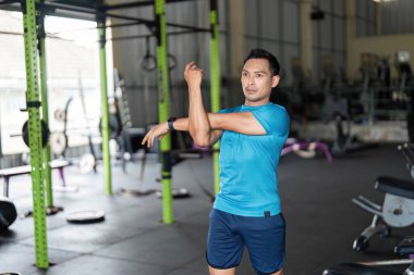 Spor salonunda kolunu uzatan kararlı bir adam spor yapmaya ve antrenmana hazırlanmaya odaklanıyor. Sağlık ve refahı vurguluyor.