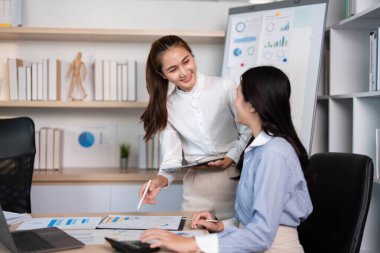 İki kadın, modern bir ofiste verileri incelerken, iş dünyasında takım çalışması ve yetkilendirmeyi desteklerken, görüşlerini paylaşıyor..