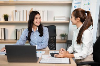 Modern bir ofiste, iki kadın stratejik bir toplantıya katılır, proje verilerini analiz eder ve etkili bir karar alma mekanizması için görüşlerini paylaşır..
