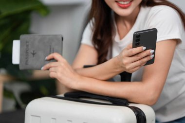 Bir kadın akıllı telefonunu kontrol ederek ve pasaportunu tutarak seyahat heyecanını ve organizasyonunu vurgulayarak yolculuğuna hazırlanır..