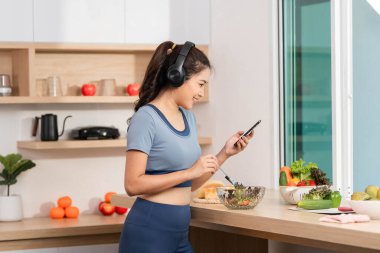 Besleyici bir salatanın tadını çıkaran genç bir kadın akıllı telefonunu kullanarak sağlık ve teknolojiyi ön plana çıkarıyor..