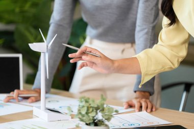 Profesyoneller ESG odaklı bir toplantıda rüzgar türbini modeli kullanarak yenilenebilir enerji çözümlerini analiz ediyorlar..