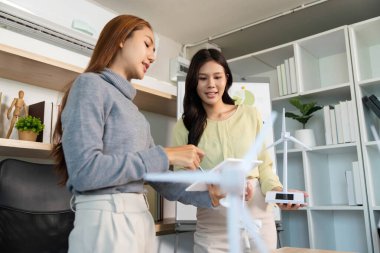 İki iş adamı, yenilenebilir enerji stratejilerini göstermek için bir rüzgar türbini modeli kullanarak ESG girişimleri hakkında bir tartışmaya girişti..