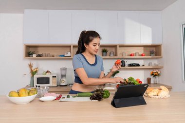 Bir kadın, taze sebze hazırlarken, sağlıklı yemek ve sürdürülebilirliği vurgularken, bir tarifi takip etmek için tablet kullanır..