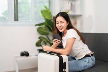 Genç bir kadın seyahat hazırlıkları için akıllı telefonunu kullanmayı sever. Planlarıyla meşgul olduğu sırada gülümser..