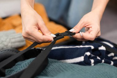 Bir kadın bavulundaki kayışları dikkatlice ayarlar, seyahati için her şeyin güvenli olduğundan emin olur. Seyahat hazırlığı ve organizasyonu kavramı.