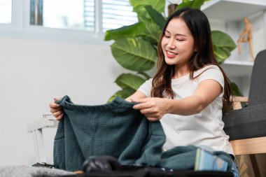 Gülümseyen bir kadın seyahat için hazırlanırken kazaklarını düzenler, seyahat için heyecanını gösterir. Hazırlık ve organizasyon kavramı.