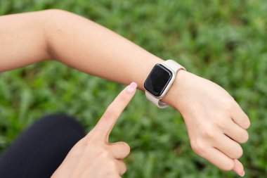 Aktif kıyafet giyen bir kadın, çimenli bir alanda yoga seansının keyfini çıkarırken sağlık ve fitness teknolojisini tanıtıyor..