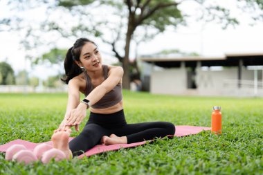 Bir kadın parkta yoga yapıyor, esnekliğini arttırmak ve rahatlamayı teşvik etmek için kollarını açıyor..