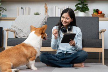 Genç bir kadın yerde oturmuş, not alırken köpeğiyle mutlu bir şekilde meşgul oluyor, evcil hayvan arkadaşlığını evde üretkenlikle harmanlıyor..