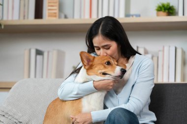 Bir kadın, Corgisine olan sevgisini nazikçe sarılarak ifade eder. Rahat bir evde duygusal bağlarının altını çizer..