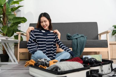 Genç bir kadın seyahat tarzını ve hazırlıklarını yansıtan çizgili bir gömlek seçerken gülümsüyor..