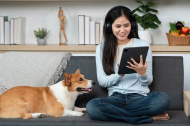 Genç bir kadın tablet kullanırken gülümsüyor, yanında Corgi köpeği oturuyor, teknolojinin ve evcil hayvan arkadaşlığının karışımını gösteriyor..