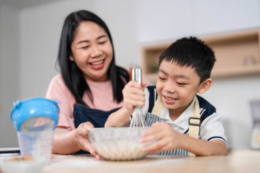 Bir anne ve oğlu yemek yapmakla meşgul, aile zamanının ve ev mutfağında yaratıcılığın keyfini vurguluyorlar..