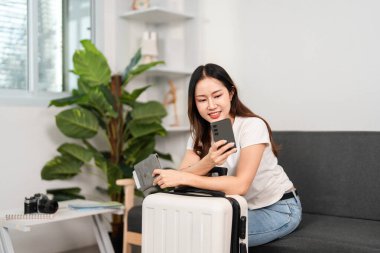 Odaklanmış bir kadın akıllı telefonuna bakar. Bagajının yanında otururken seyahat detaylarını planlar..