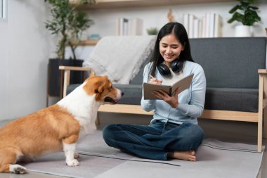 Genç bir kadın yerde oturuyor, defterine Corgi 'si yakınlardayken yazıyor. Bu sahne evcil hayvan arkadaşlığının ve yaratıcılığın neşesini yakalar..
