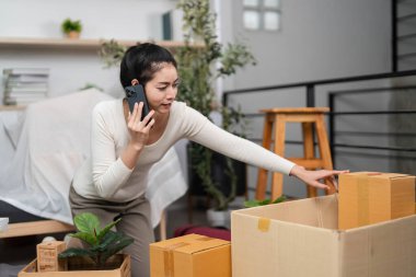 Telefondaki bir kadın, taşınma sürecini aktif olarak yönetiyor, şık bir evde paketsiz kutular ve bitkilerle çevrili..