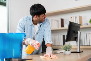 Modern ofis ortamında masayı özenle temizleyen genç bir adam temizlik ve organizasyona bağlılığını gösteriyor..