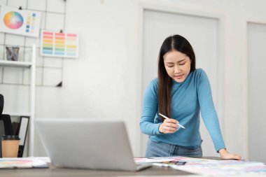 Modern bir çalışma alanında, bir tasarımcı canlı renk paletleri ve dijital tasarımları inceleyerek yaratıcılığını ve detaylara olan ilgisini gösterir.