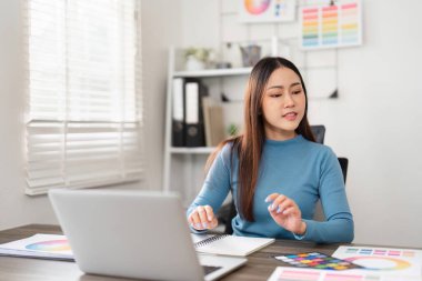 Huzurlu bir çalışma alanında, genç bir tasarımcı yaratıcılık ve tasarım sunumuna hazırlanan renk şemaları ve örnekleri inceler..