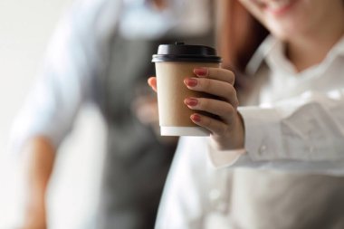 Parlak bir gülümseme ile, barista sürdürülebilir bir kahve fincanını neşeli bir müşteriye teslim eder, yeşil bir kahve dükkanında dostluk hizmetinin özünü yakalar..