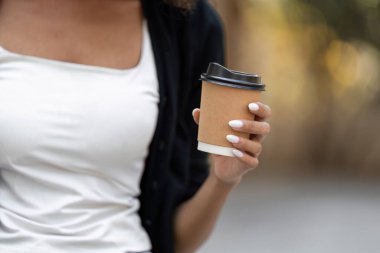 Bir kadın açık havada gününün tadını çıkarırken elinde sürdürülebilir bir kahve fincanı tutarak çevre dostu tercihlere olan bağlılığını vurgular..