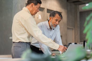 İki deneyimli adam, modern bir iş ortamında işbirliği ve stratejik planlamayı vurgulayarak bir dizüstü bilgisayarda verileri incelerken aynı fikirleri paylaşıyor..