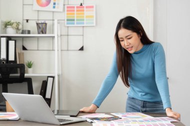 Bir kadın tasarımcı masasındaki renk örneklerini ve tasarım materyallerini inceleyerek çağdaş ofis ortamındaki yaratıcı projesine derinden odaklanır..