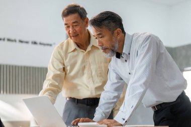 Yaşlı bir müşteri ve danışman, stratejik iş planlaması ve sorun çözme üzerine yoğunlaşarak, bir dizüstü bilgisayarın üzerinde işbirliği içinde çalışırlar..