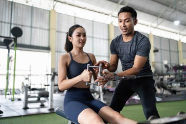 Kişisel antrenör, kürek çekme tekniğini bayan bir müşteriye açıklar. Spor salonunda etkili bir egzersiz performansı sağlar..