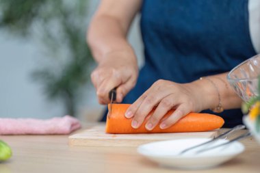 Bir havucu ustalıkla keserken, şık bir mutfak ortamında sağlıklı yemek hazırlığını vurguluyor..