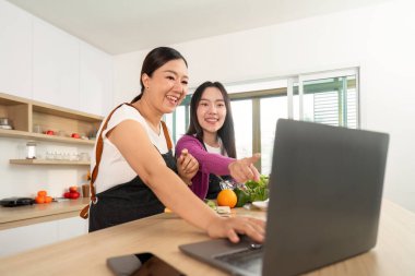 Günümüz mutfağında, teknolojiyi aşçılıkla harmanlayan iki kadın, yemek tarifi için dizüstü bilgisayar kullanırken keyifli bir anı paylaşıyor..