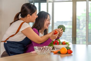 Neşeli bir mutfak ortamında sağlıklı yemekleri taze sebzelerle hazırlarken iki kadın aynı kahkahayı paylaşıyor..