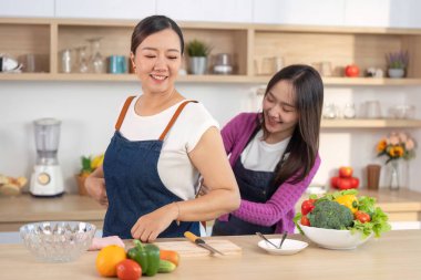 İki kadın, modern bir mutfakta, taze sebzeler hazırlayıp birbirlerine eşlik ederek, keyifli bir yemek pişirme deneyimini paylaşıyor..