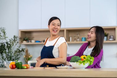 İki arkadaş, çağdaş bir mutfakta taze sebzelerle sağlıklı yemekler hazırlarken keyifli bir anı paylaşıyorlar..