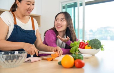 Mutfakta neşeli bir an. İki kadın sebze doğruyor ve sağlıklı yemek yaparken bağ kuruyor. Sağlık ve sağlıklı yaşam tarzına vurgu.