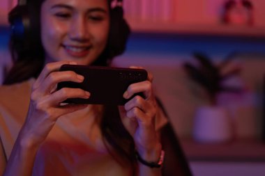 Kulaklıklı genç bir kadın gezici bir oyun oynarken gülümsüyor, renkli ve rahat bir ortamda zevkini yansıtıyor..