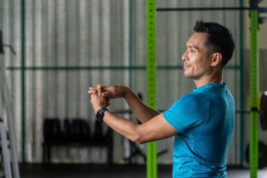 Mavi atletik gömlekli bir adam spor salonunda kollarını uzatarak antrenmana hazırlanıyor. Forma ve sağlığa odaklan..