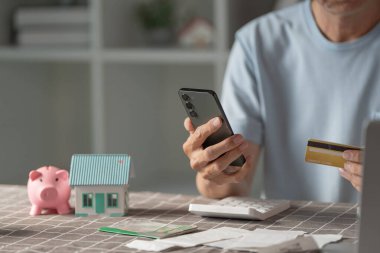 Mali yetkilendirme ve dijital araçları vurgulayarak, evde akıllı telefon ve kredi kartı kullanarak finansman yönetiyor.