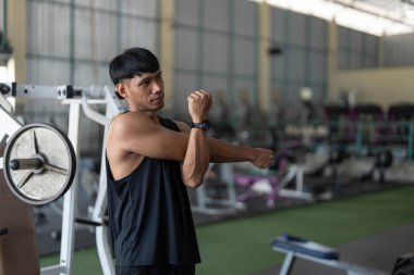 Siyah kolsuz tişörtlü bir adam spor salonunda kollarını uzatıyor, antrenmandan önce esneklik ve forma odaklanıyor..