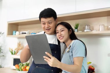 Modern bir mutfakta tablete bakarken birkaç gülümseme, keyifli bir yemek pişirme anını paylaşıyor. Sağlıklı yemek yapmaya odaklan..