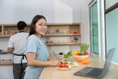 Parlak bir mutfakta taze sebzeler hazırlarken gülümseyen bir kadın sağlıklı yemek ve neşe sunar..