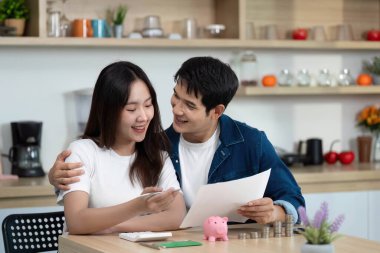 Bir çift, kumbaralarını elinde tutarken mali belgelerini neşe içinde gözden geçirip tasarruf yapmaya çalışıyor..