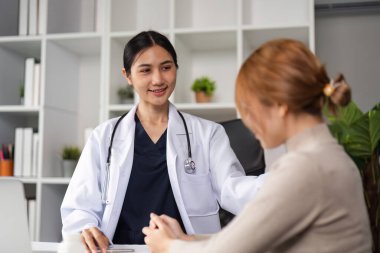 Beyaz önlüklü bir kadın doktor, modern bir muayenehanedeki hastaya sağlık ve profesyonelliği vurgulayarak sağlık tavsiyesinde bulunuyor..