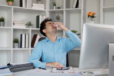 Stresli bir işçi, yoğun bir ofis ortamında sağlık sorunlarını gösteren grip belirtileriyle boğuşuyor..