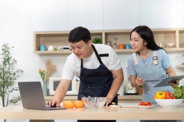 Bir çift, modern bir mutfakta taze malzemeler hazırlarken dizüstü bilgisayarda yemek tarifleri keşfediyor. Sağlıklı yemek yapmaya odaklan..
