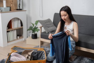 Genç bir kadın seyahat macerasına hazırlanmak için bavulunu topluyor. Konforlu, modern bir oturma odasında giysi ve gerekli şeyleri organize ediyor..